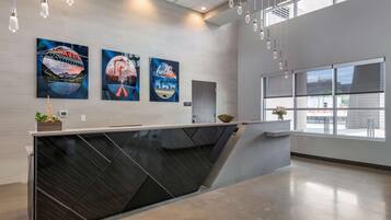 A modern reception desk with a dark, angular design, large windows offering views of the outside, and three travel-themed artworks on the wall.