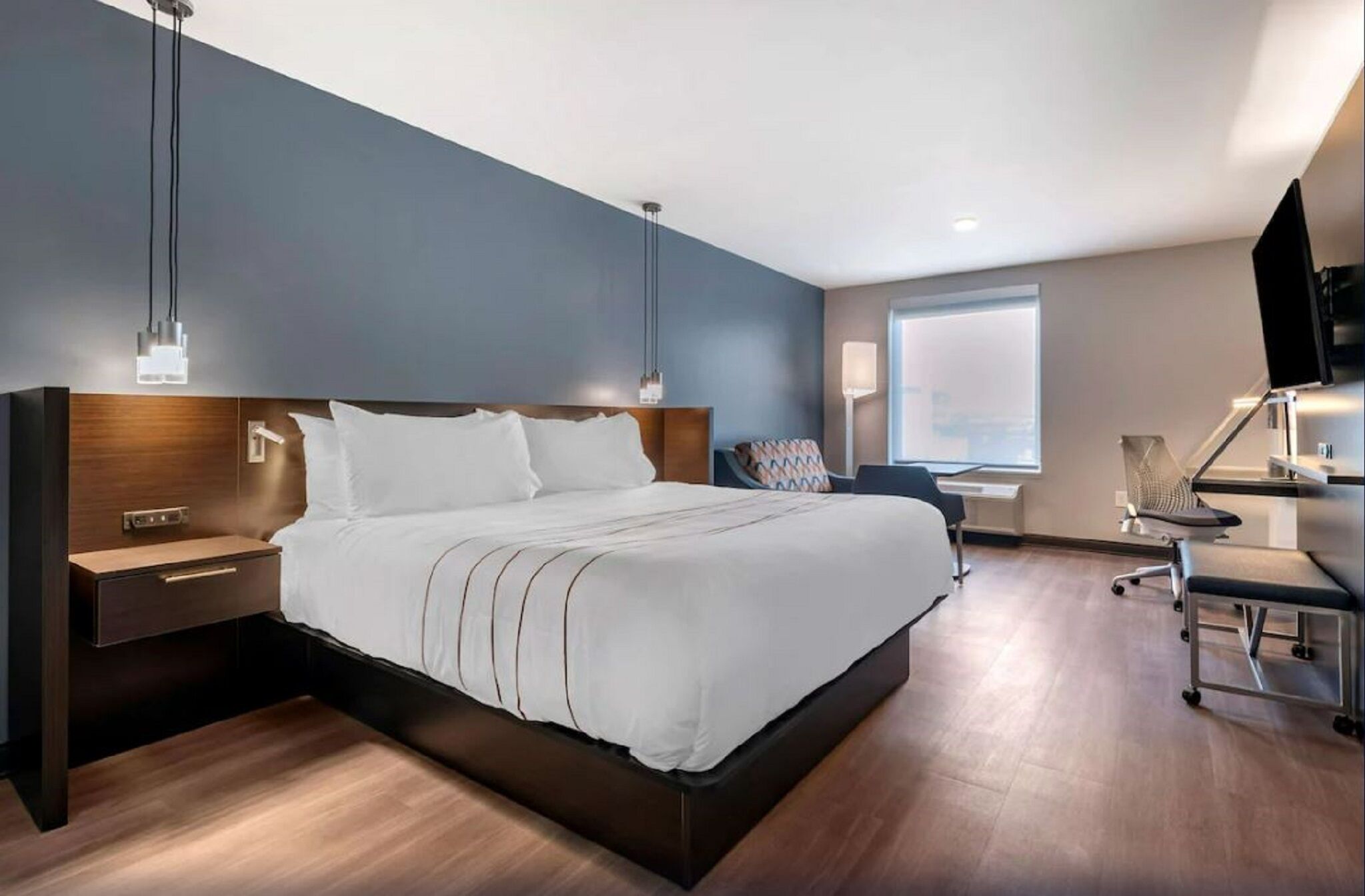 Ein modernes Hotelzimmer mit einem großen Bett, Nachttischen, einem Schreibtisch und einem Sessel.