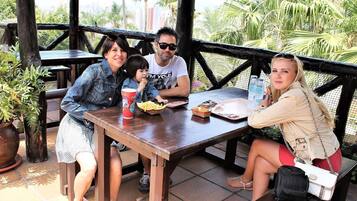 A group of people seated at an outdoor wooden table with a view of palm trees and buildings in the background.