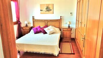 A bedroom with a wooden bed, two bedside tables with lamps, a wooden wardrobe, and a painting on the wall.