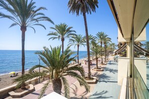 Un balcón con vistas a la playa y al océano, palmeras y un edificio de diseño moderno.