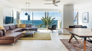 A modern living room with a large window, a ceiling fan, a brown leather sofa, a coffee table, and a dining table. - Apartment 'Great First Line Amazing Terrace' with Sea View, Wi-Fi and Air Conditioning (Marbella)
