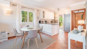 Una cocina moderna con armarios blancos, una mesa de comedor con sillas y vistas a la vegetación.