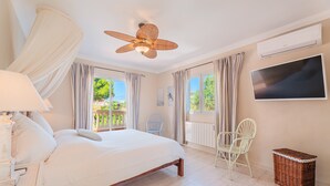 Un dormitorio con cama, ventilador de techo, televisor y vistas al exterior.
