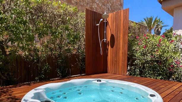 Un jacuzzi en una terraza de madera, con una valla de madera y follaje al fondo.