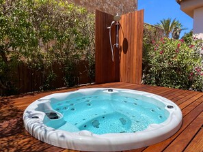 Ein Whirlpool auf einer Holzdiele mit Holzzaun und Grünpflanzen im Hintergrund.