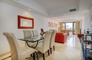 Un salon moderne avec une table à manger en verre, des fauteuils en cuir, un canapé rouge et une grande fenêtre offrant une vue dégagée.