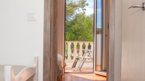 Une porte ouverte donnant sur un balcon d’où l’on peut admirer les arbres, le balcon étant agrémenté d’une balustrade blanche.