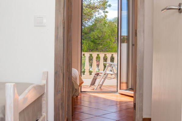 An open door leading to a balcony with a view of trees and a white railing.