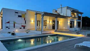 Una casa moderna de dos pisos con piscina, mobiliario exterior y un patio bien iluminado.