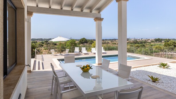 Un espacio al aire libre techado con piscina, sillas de descanso y una mesa con un frutero.