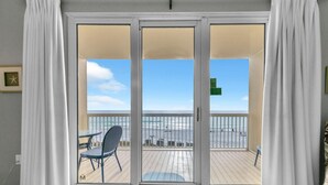 A room with a sliding glass door leading to a balcony with a view of the beach and ocean.