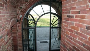 Un arco de ladrillo que da paso a un patio con una reja y vistas a un campo verde.