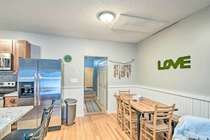 A modern kitchen with stainless steel appliances, a dining area with wooden furniture, and a wall with a 'LOVE' decoration. - Near Newfound Lake: Plymouth Condo w/ Fireplace! (Plymouth)