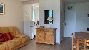 A living room with a sofa, wooden cabinet, and a dining area with a table and chairs. - Bright 1-bedroom apartment, south balcony, for 6, in Pra Loup 1500 (Pra-Loup)
