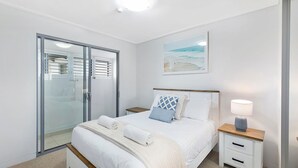 Een slaapkamer met een bed, nachtkastjes, een lamp, een schilderij en een schuifdeur.'