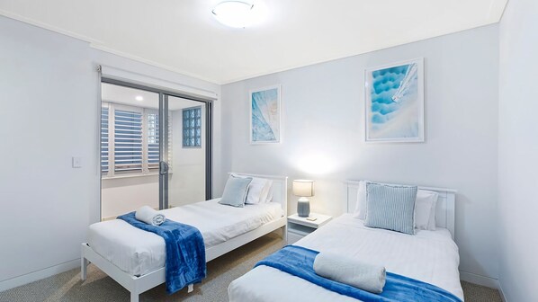 Habitación de hotel con dos camas, una puerta corrediza, una mesita de noche con lámpara y obras de arte en las paredes.