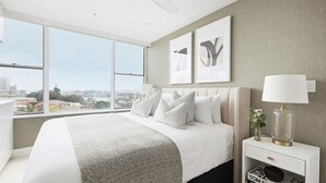 Une chambre à coucher moderne avec un grand lit, une table de chevet avec une lampe et des œuvres d’art accrochées au mur.