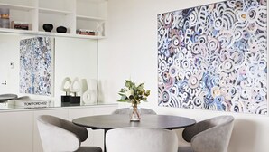 Un intérieur moderne avec une table ronde, des chaises recouvertes d’un tissu gris, un vase agrémenté de plantes et des œuvres d’art abstraites accrochées aux murs.