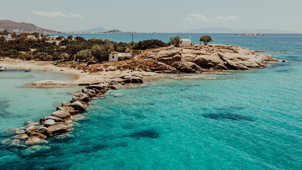 Eine Küstenlandschaft mit klarem türkisblauem Wasser, felsigem Ufer und einer kleinen Siedlung mit Gebäuden und Bäumen.