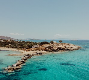 Paisagem costeira com águas turquesa cristalinas, linha costeira rochosa e um pequeno povoado com edifícios e árvores.