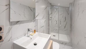 Une salle de bain moderne avec un grand miroir, un lavabo blanc, une douche en verre et des toilettes.