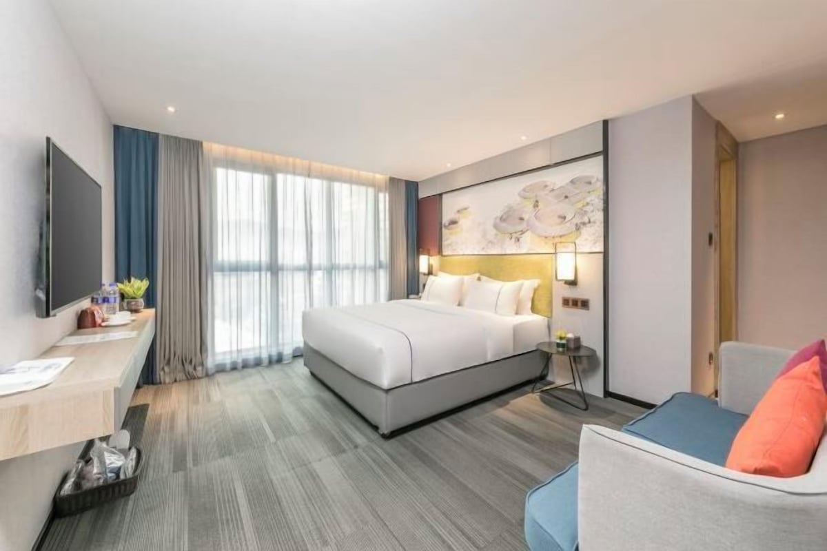 Ein modernes Hotelzimmer mit einem großen Bett, einem Schreibtisch, einem Stuhl und einem Fernseher.