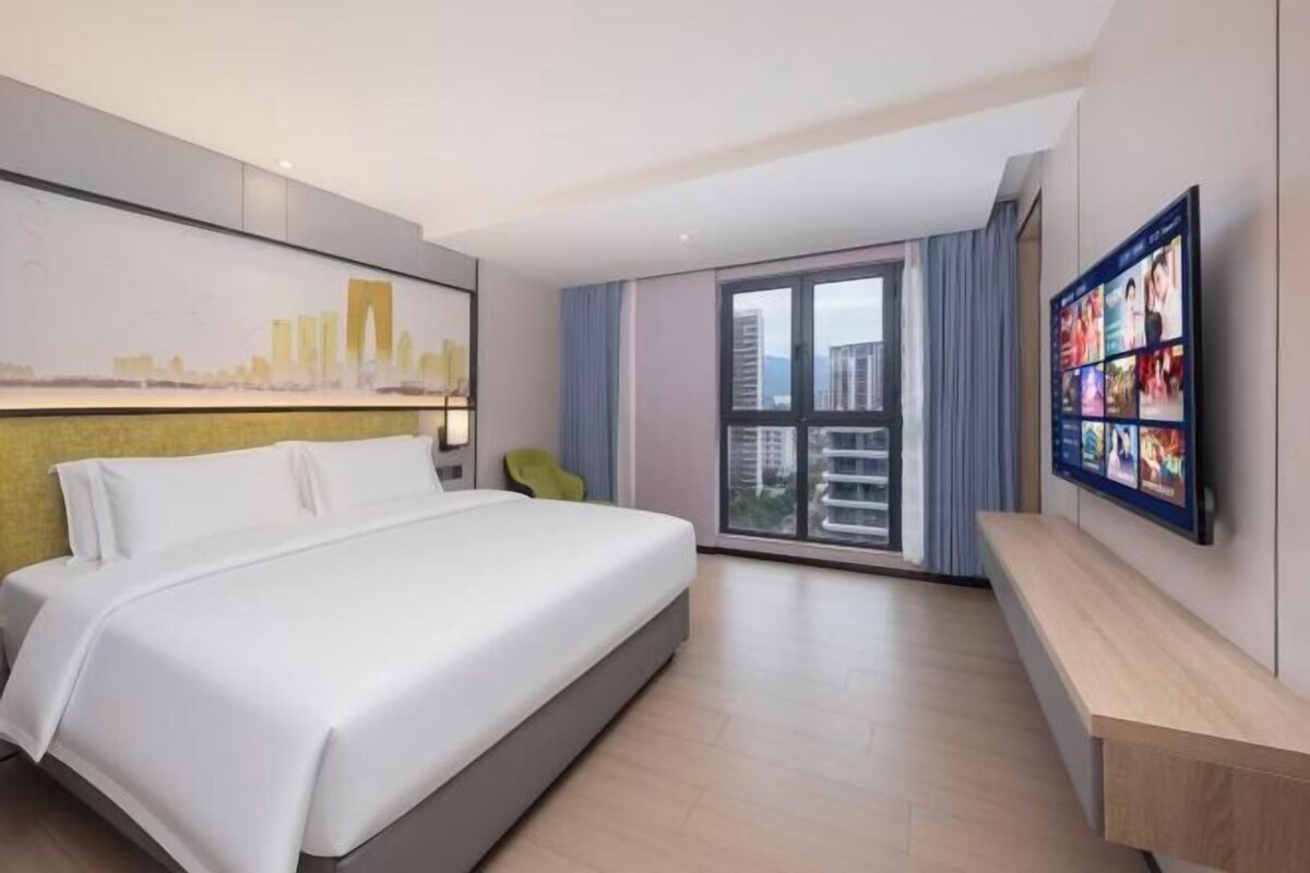 Una habitación de hotel moderna con una cama grande, un cuadro de un paisaje urbano, un televisor y un balcón con vistas a rascacielos.