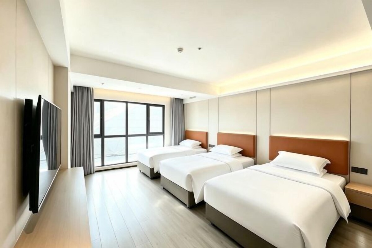 Habitación de hotel con tres camas, un televisor y un ventanal grande.