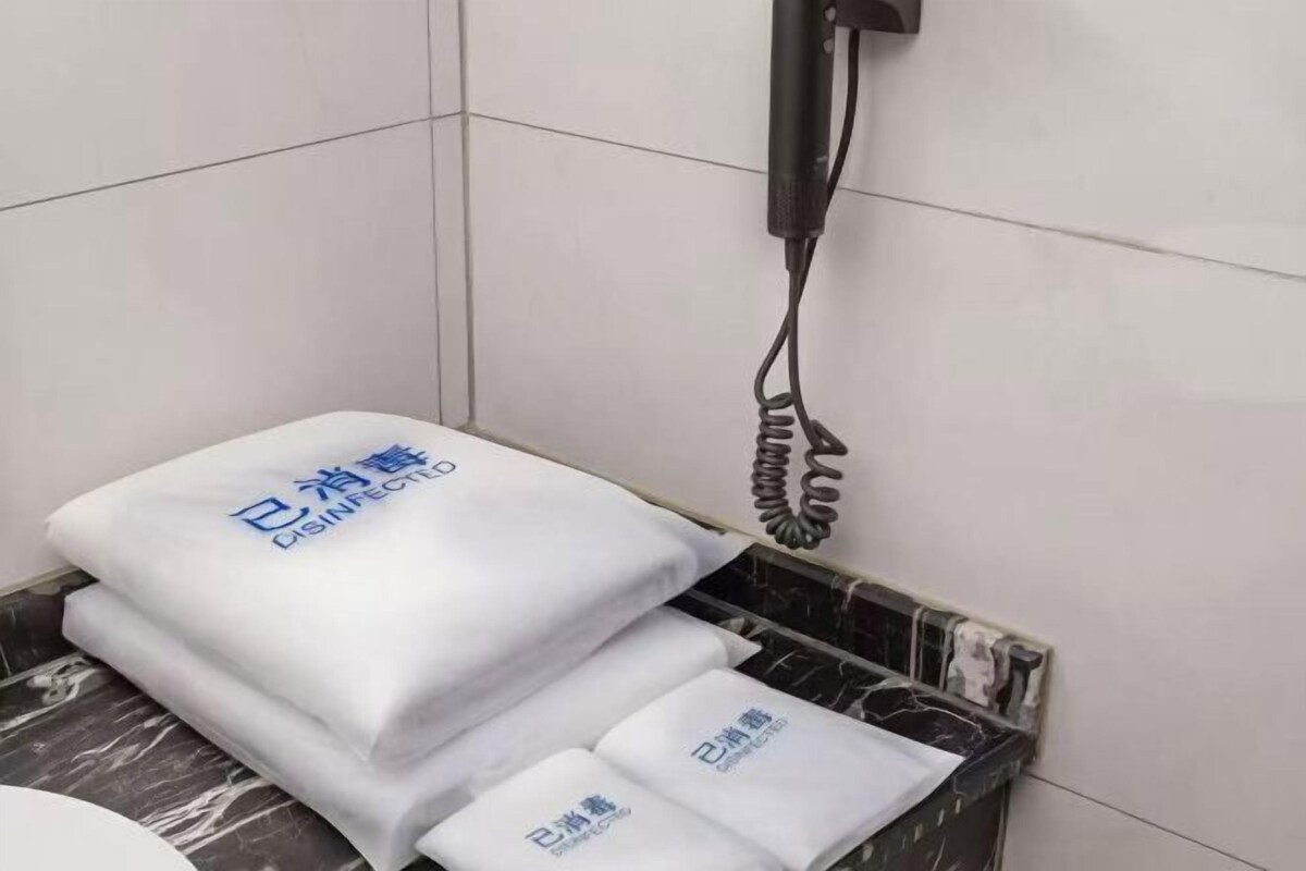 Un baño con un lavabo de mármol, un dispensador de toallas blanco con texto azul, y un teléfono negro montado en la pared.