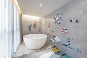 A modern bathroom with a large freestanding bathtub, nautical-themed wall art, and a small table with towels.