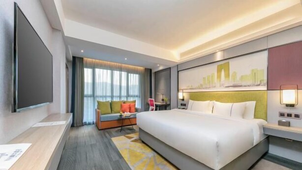 A hotel room with a large bed, a desk, a sofa, and a cityscape painting on the wall. - Maple, Longyan, Wanda Plaza (Longyan)