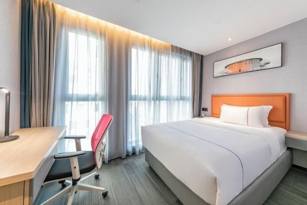 Ein Hotelzimmer mit einem großen Bett, einem Schreibtisch mit Stuhl und einem fensterbepflanzten Fenster.