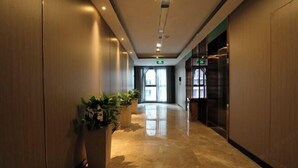 A modern hotel corridor with polished marble floors, wooden paneling, and potted plants. - Maple, Longyan, Wanda Plaza (Longyan)