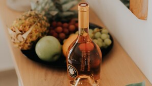 Een fles Miraval Provence op een houten plank met verschillende soorten fruit en een groen blad.