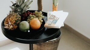 Een klein tafeltje met een fruitschaal met ananas, druiven, een sinaasappel en een limoen, naast een bloempot.