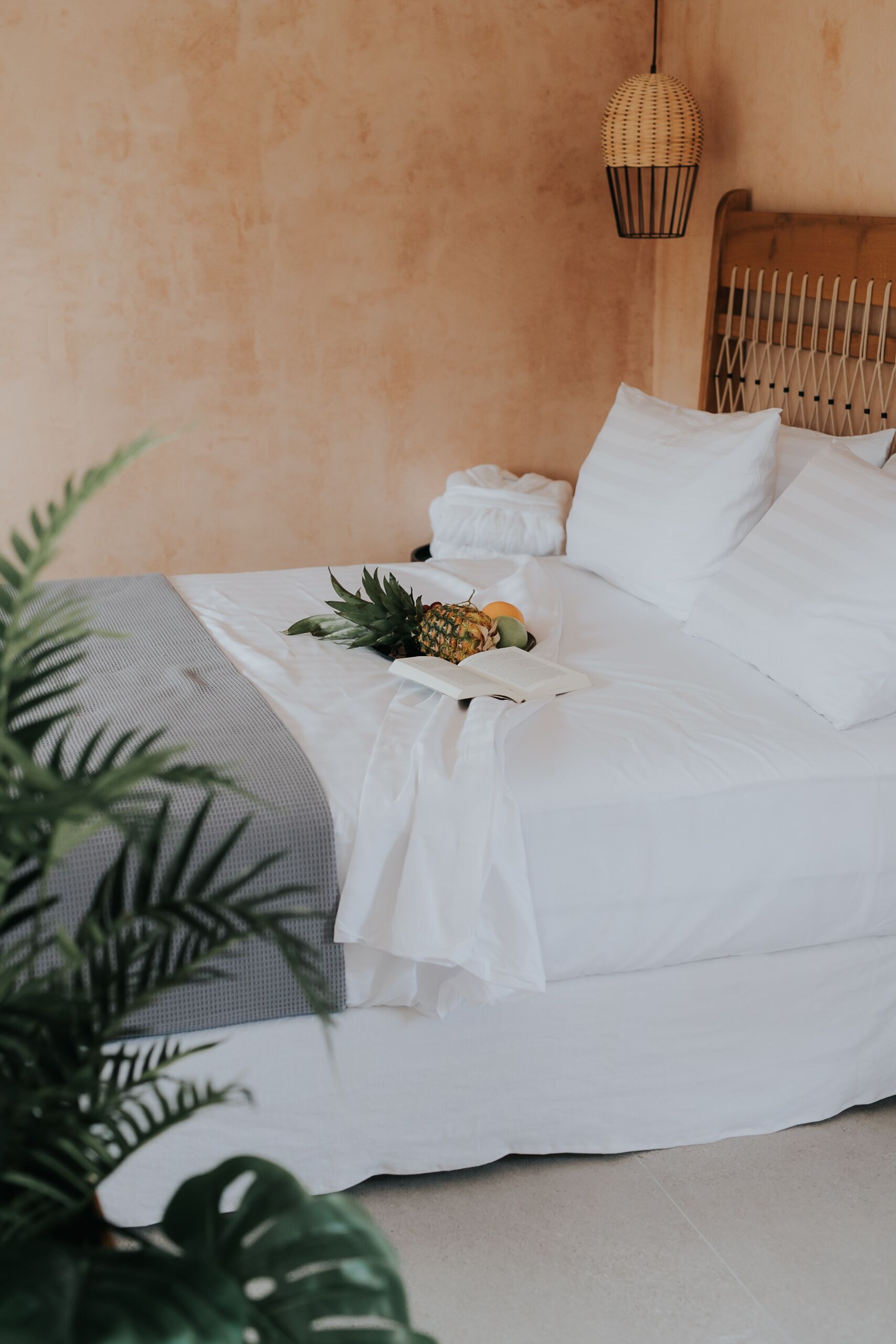 Un lit bien fait, avec des draps blancs, un ananas et un livre posés dessus.