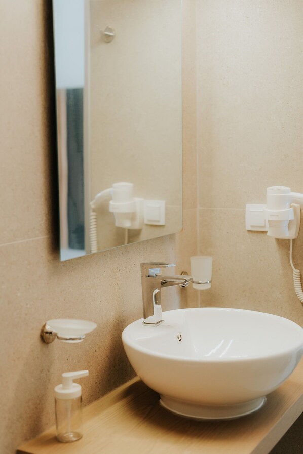 A bathroom with a white sink, a mirror, a towel dispenser, and a hairdryer on the wall. - Elia Boutique Hotel (Parga)