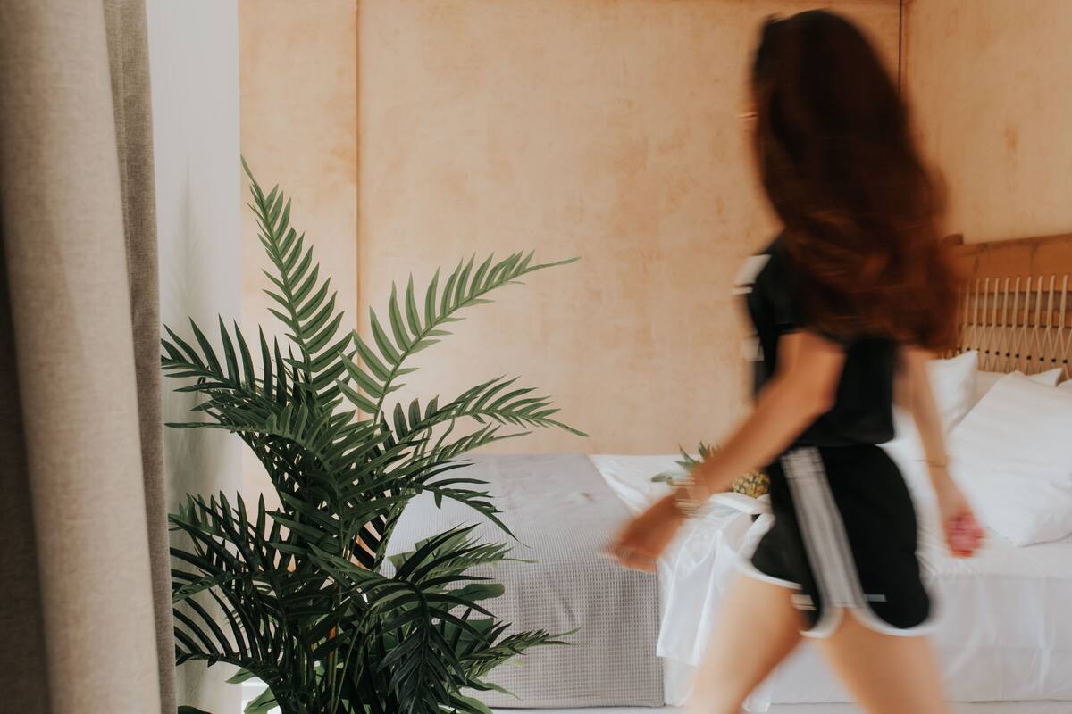 A room with a bed, a potted plant, and a person walking.