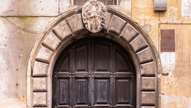 A large, ornate wooden door with a stone archway, set in a weathered building facade. - Historical Apartment few steps from Piazza Navona (Roma)