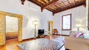 A spacious room with a wooden ceiling, a large mirror, a television, a sofa, and a patterned table. - Historical Apartment few steps from Piazza Navona (Roma)
