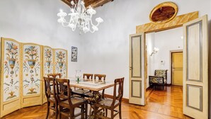 A dining area with a wooden table and chairs, a chandelier, and a decorative screen with floral patterns. - Historical Apartment few steps from Piazza Navona (Roma)