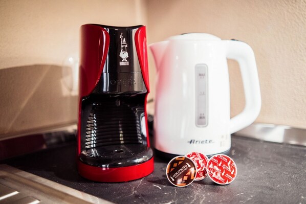 Una cafetera roja y negra y una tetera eléctrica blanca sobre una encimera.