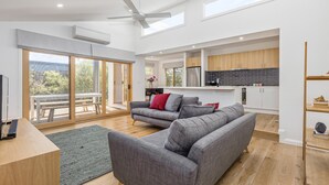 A spacious living area with a grey sofa, a wooden dining table, and a large sliding glass door leading to an outdoor patio.