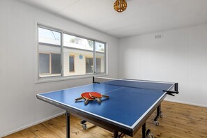 A ping pong table with two paddles in a room with white walls, a window, and a wooden floor.
