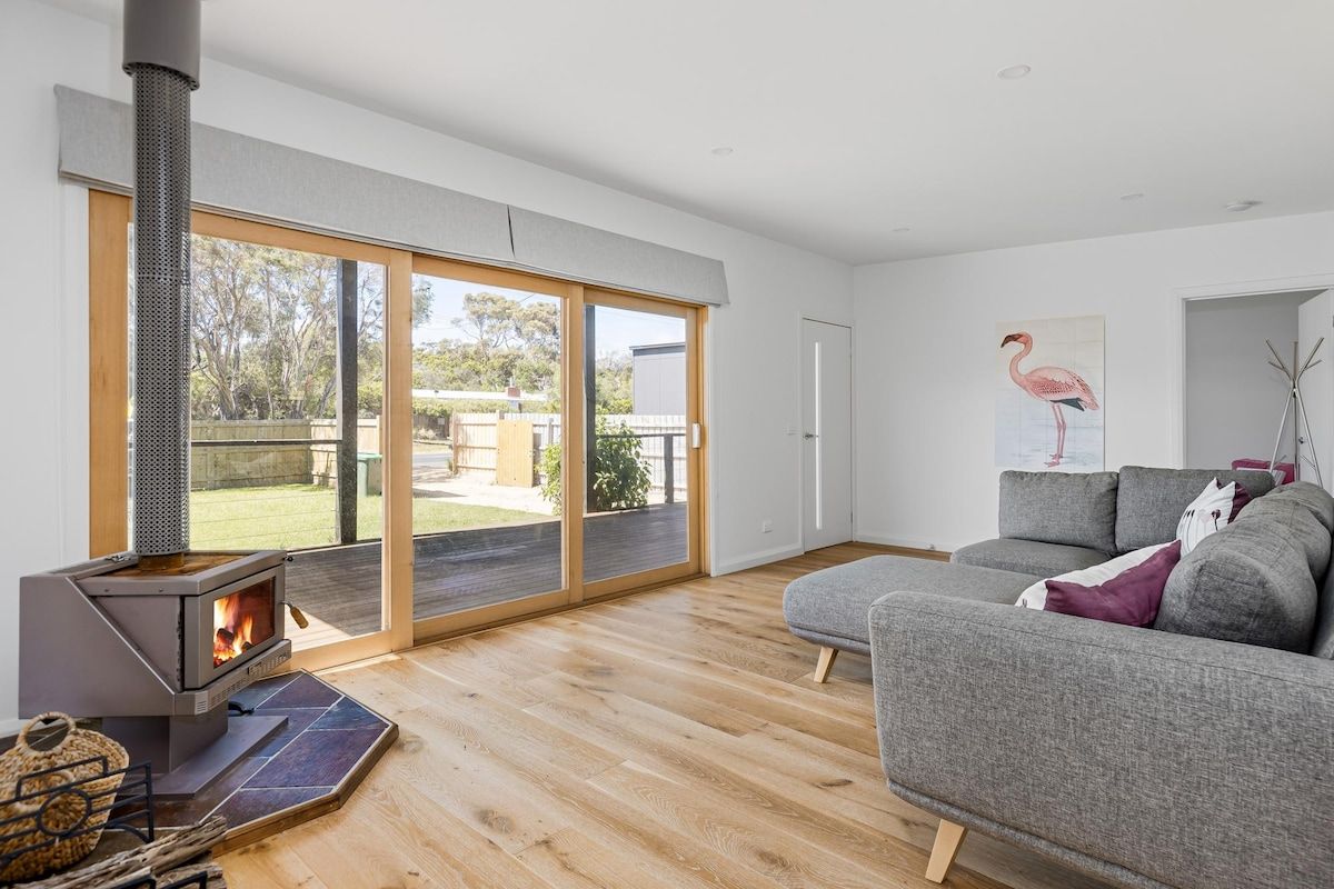 A modern living room with a wood-burning stove, a grey sofa, and a large sliding glass door leading to an outdoor area.
