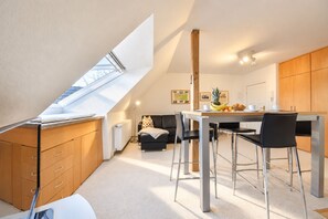 A compact kitchen with a dining area, a loft bedroom with a skylight, and a small living space with a sofa and a coffee table.