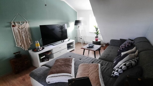 A living room with a flat-screen TV, a sofa, a coffee table, and a lamp. - Apartment in a central location (06502 Thale OT Westerhausen)