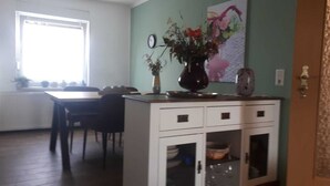 A dining area with a table and chairs, a white cabinet with drawers, and a vase with flowers on top. - Apartment in a central location (06502 Thale OT Westerhausen)