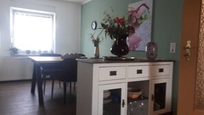A dining area with a table and chairs, a white cabinet with drawers, and a vase with flowers on top.